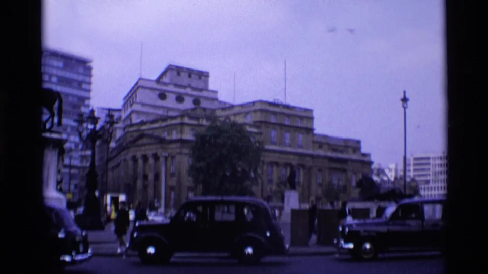 1969 London street view with black taxis, pedestrians, a grand classical building, lamp posts, and modern blocks in the background.