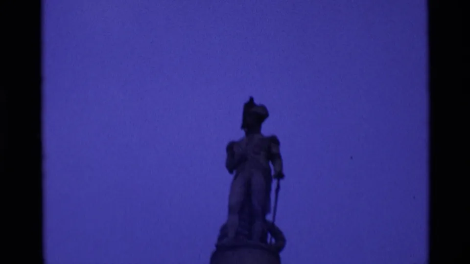 Blue-toned 1969 London 8mm frame with a distant robed statue on a pedestal framed against open sky.