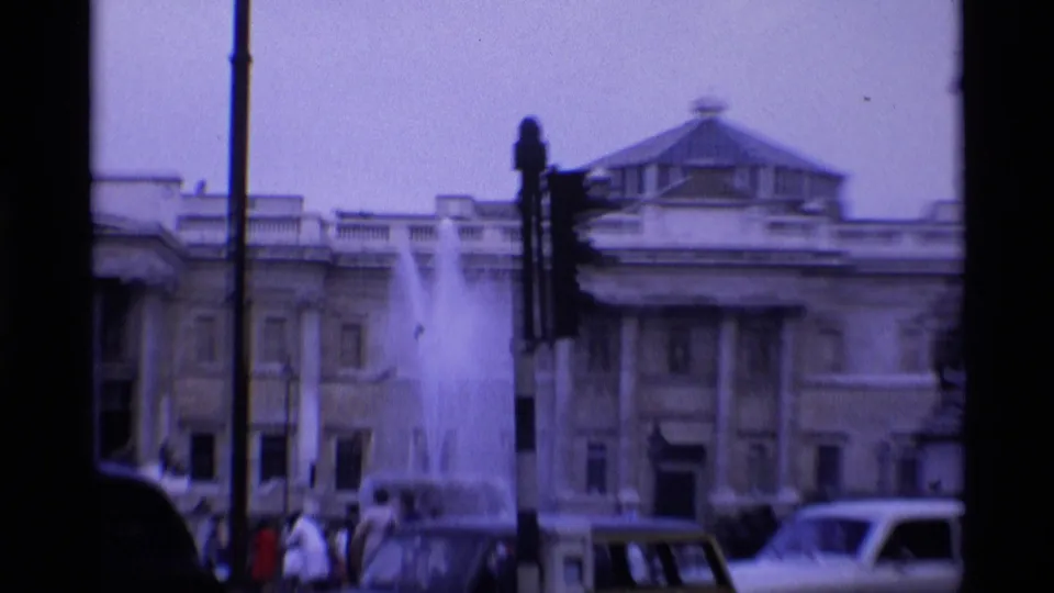 1969 Trafalgar Square view with fountain spray, National Gallery facade, traffic lights, cars, pedestrians, and a red bus.