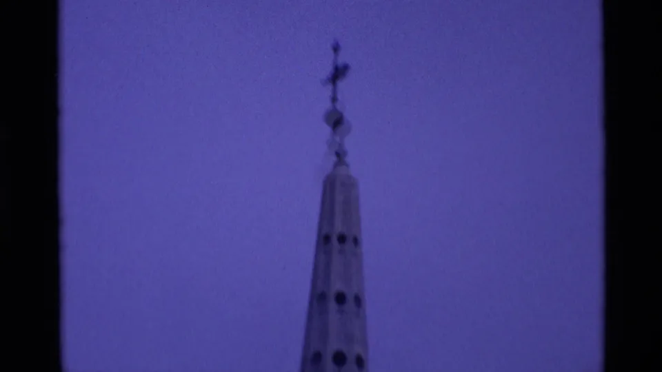 1969 London 8mm frame isolating a tall steeple topped with a weather vane or finial against the purple-tinted sky.