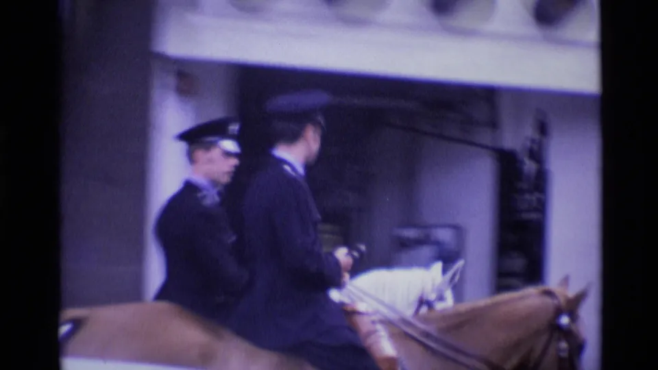 Two uniformed mounted police officers on horseback are filmed close-up near a London building entrance in 1969 8mm footage.