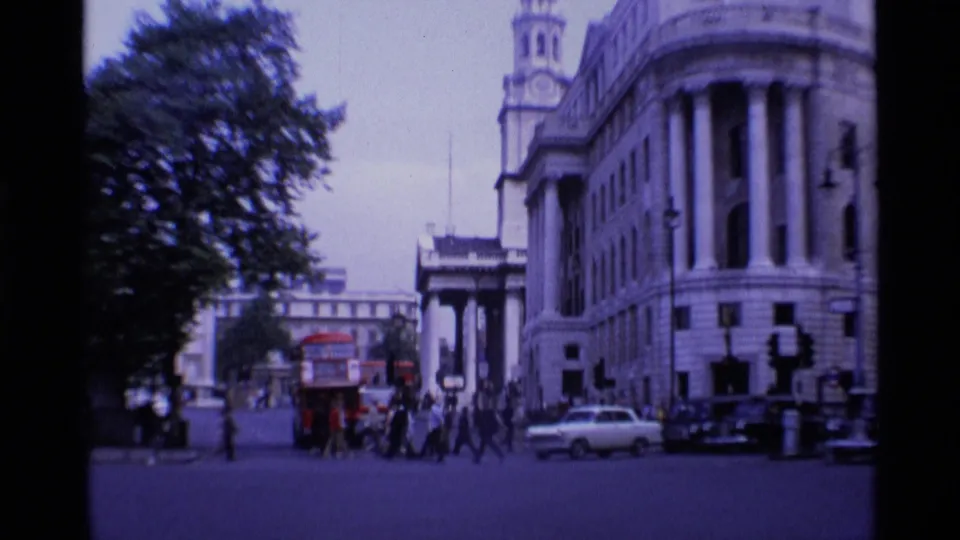 A wide London street scene shows pedestrians, vintage cars, a red bus, and the spire of St. Martin-in-the-Fields in 1969.
