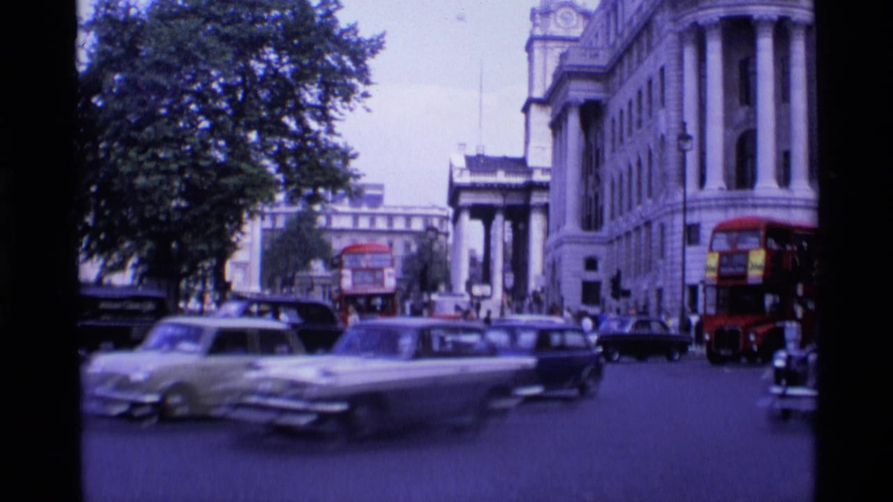 1969 London street view with red double-decker buses, vintage cars, a black taxi, pedestrians, trees, and a grand stone building.