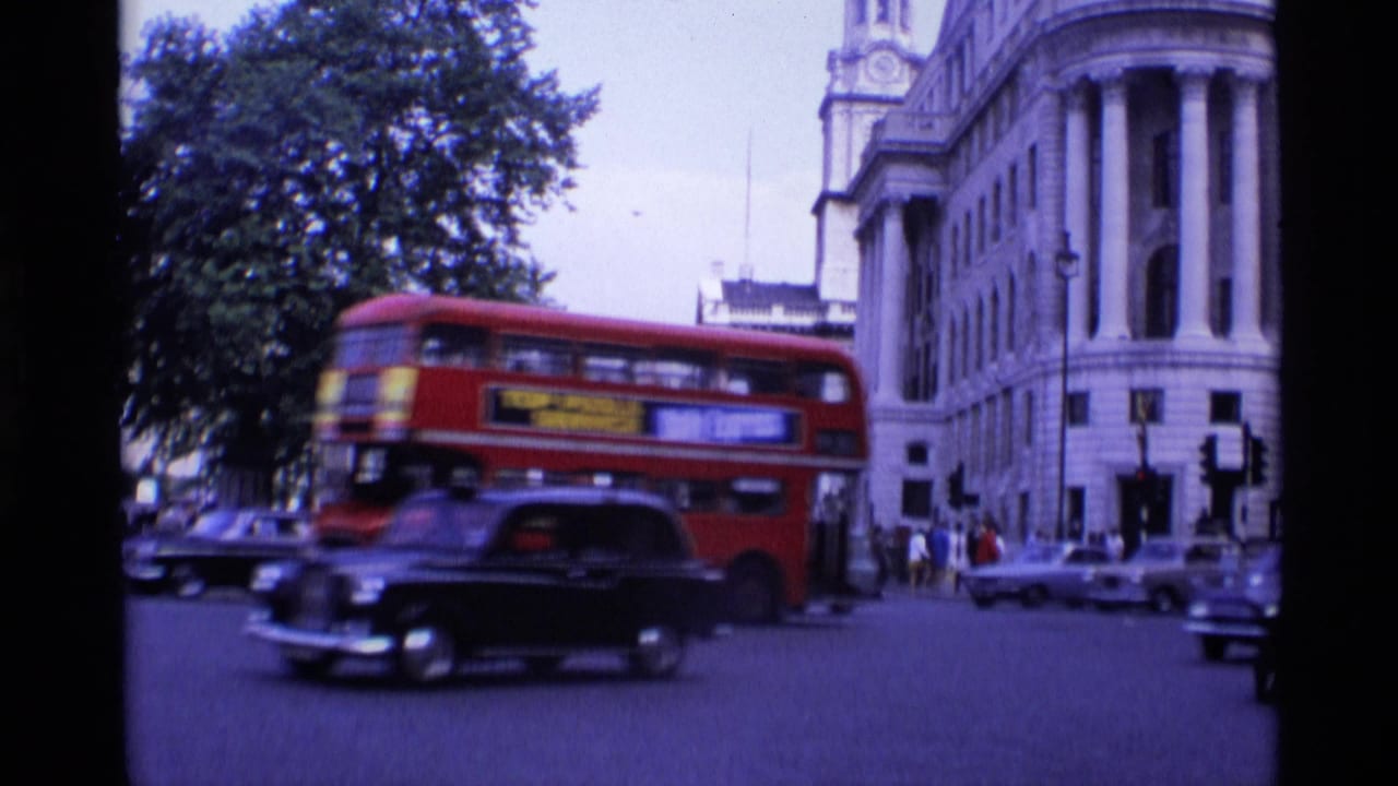 Red double-decker bus and black taxi moving through an intersection beside a large stone building.