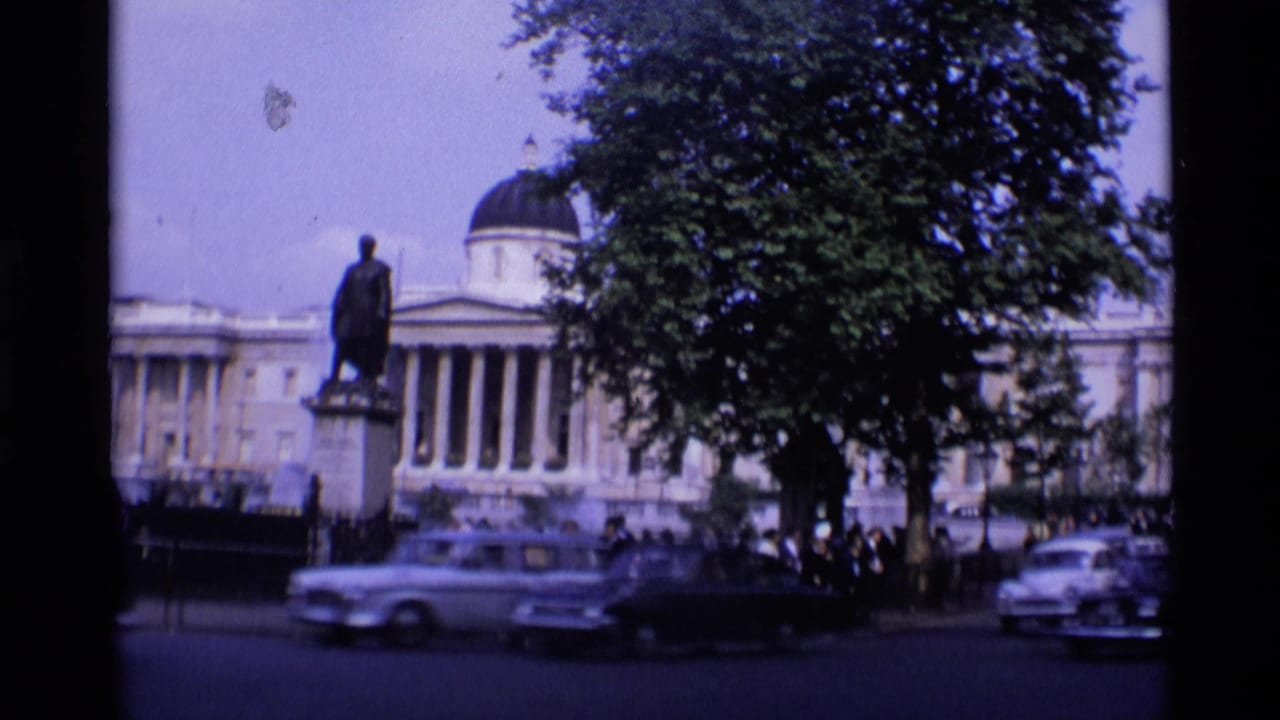 1969 London street view with a domed neoclassical building, statue, tree cover, passing cars, and pedestrians in the distance.