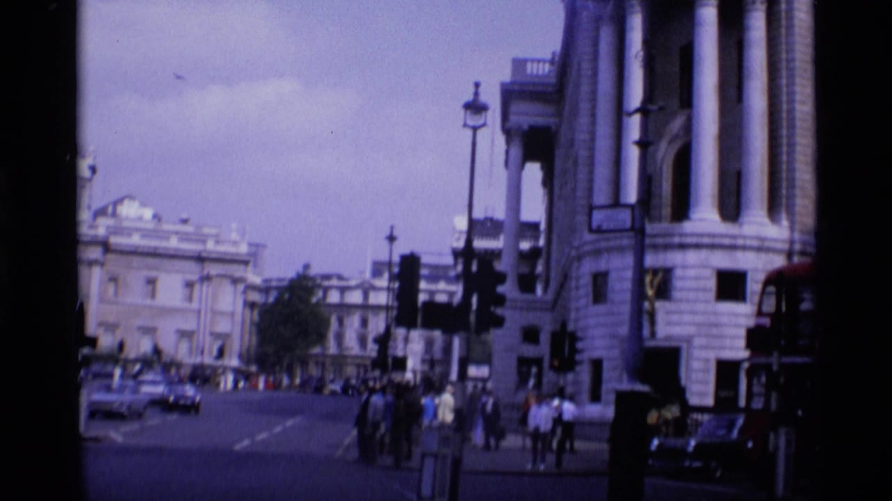 City street corner with stone buildings, traffic signals, pedestrians, and cars.
