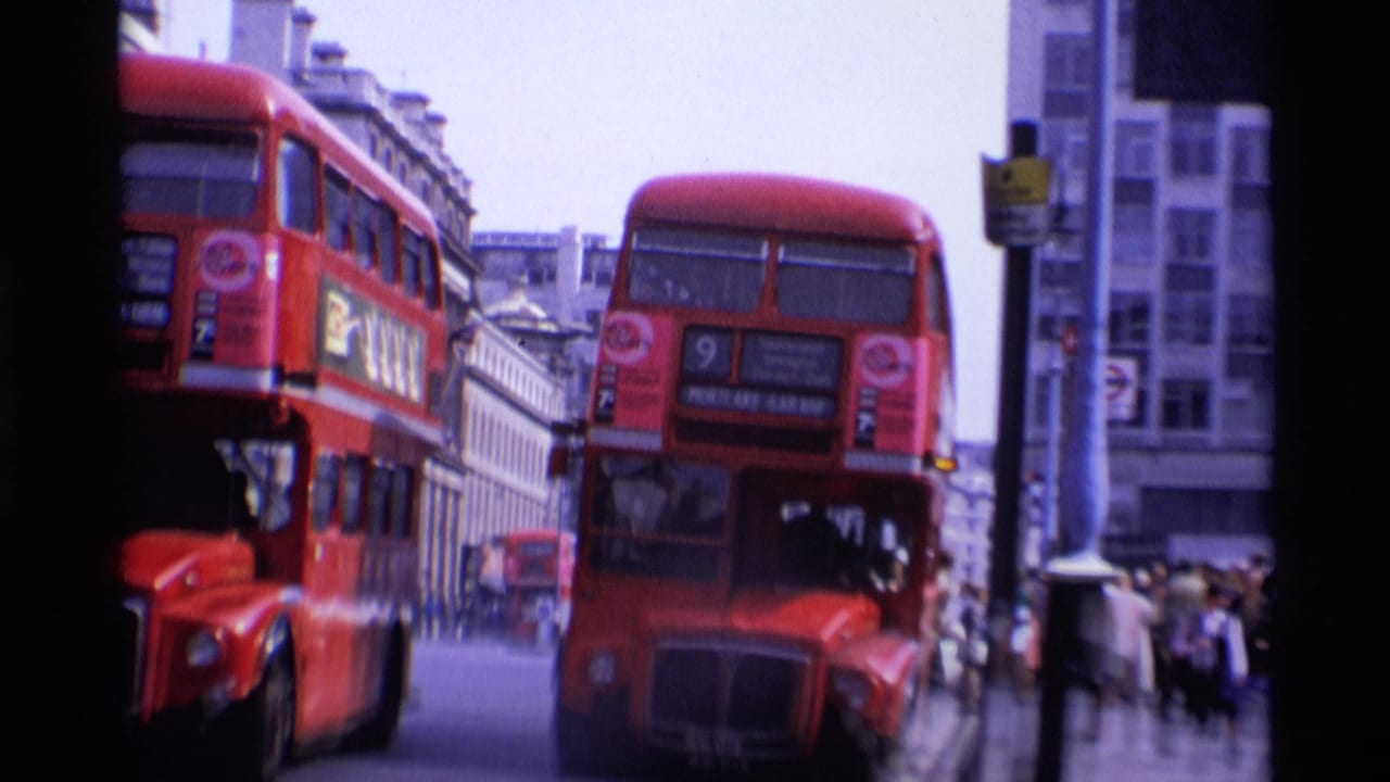 1969 London street view with red double-decker buses passing close to the camera and pedestrians near city buildings.