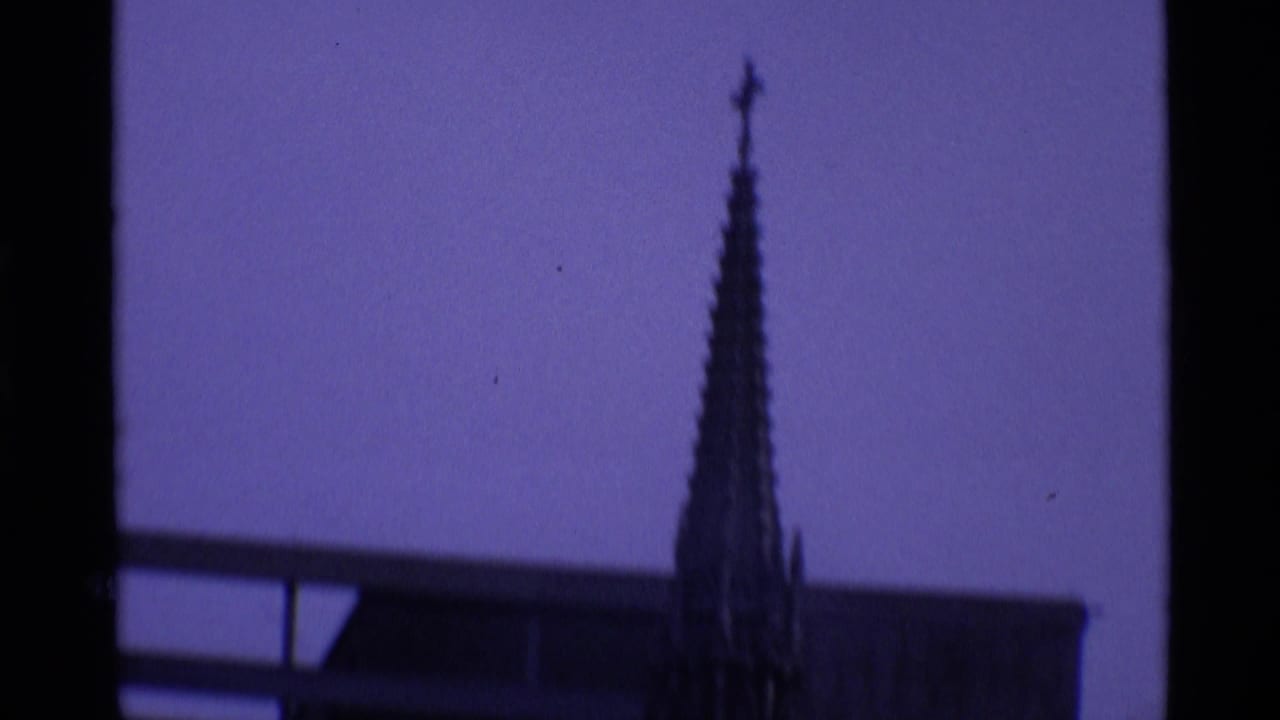 Dark Gothic-style spire or monument silhouette against a purple-tinted sky and building roofline.