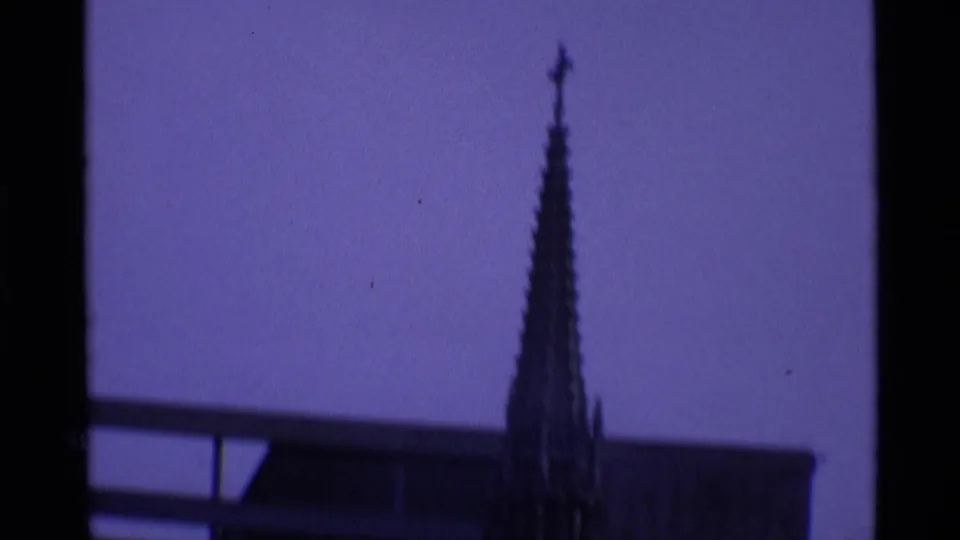 Handheld London landmark cutaway showing a narrow Gothic-style spire or monument detail against a purple-blue sky.