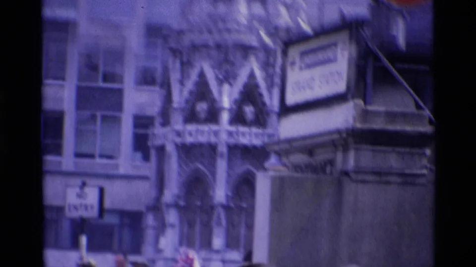 Close London landmark view with ornate monument architecture, nearby signage, and office windows in 1969 home-movie color.