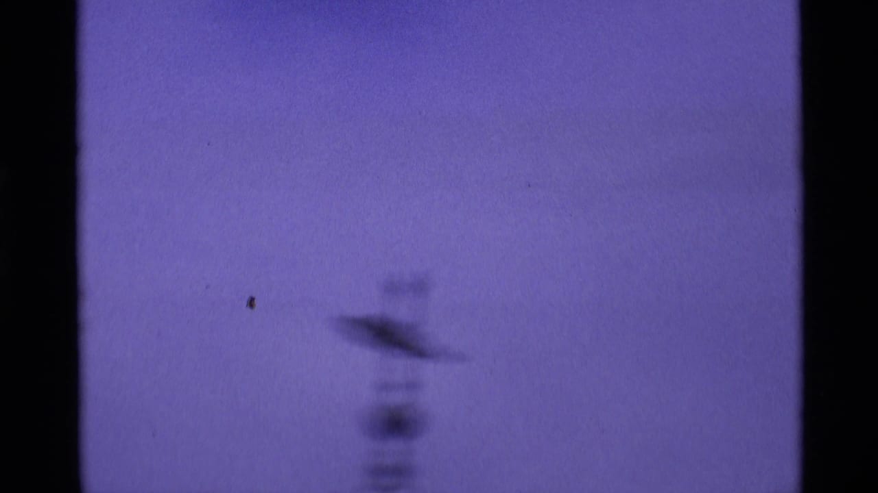 London 1969 home-movie frame with a soft, blurred tower form against a blue-purple sky and dark 8mm frame edge.