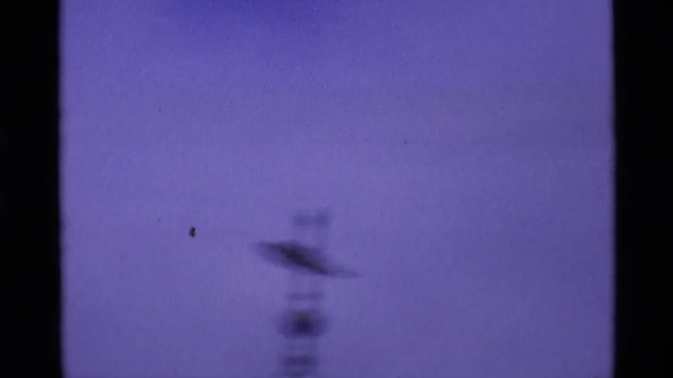 London 1969 home-movie frame with a soft, blurred tower form against a blue-purple sky and dark 8mm frame edge.