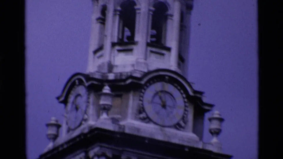 Historic London clock tower detail from a 1969 8mm home movie, showing clock faces, arches, and ornate stonework.