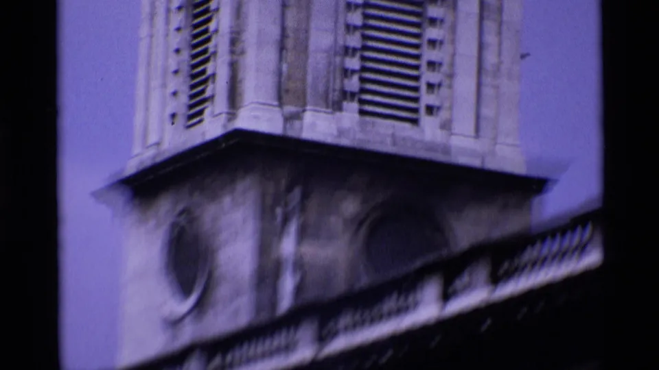 London 1969 8mm frame of a stone tower with louvered openings, a round window, and dark roofline crossing the lower view.