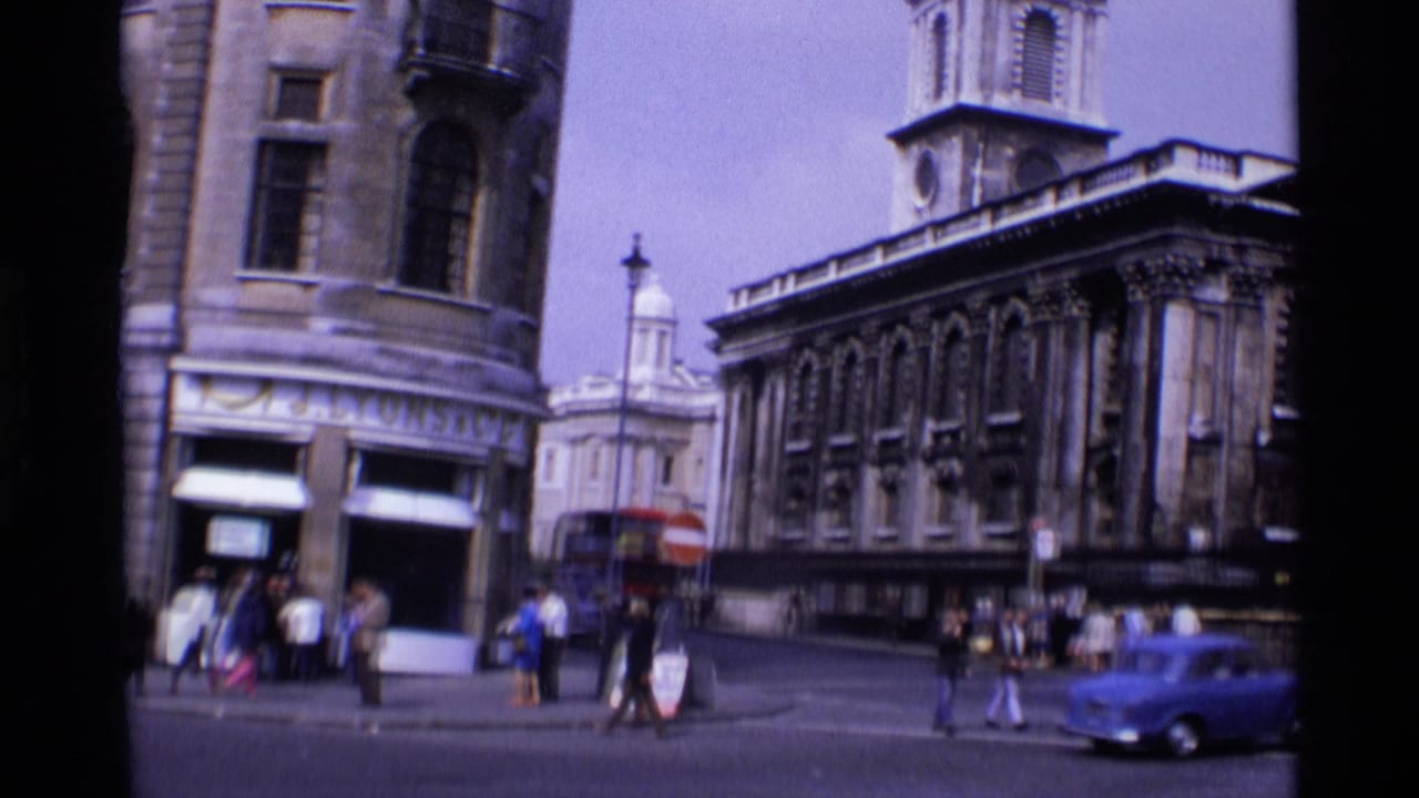 Street corner with historic buildings, pedestrians, a red bus, and a blue car.