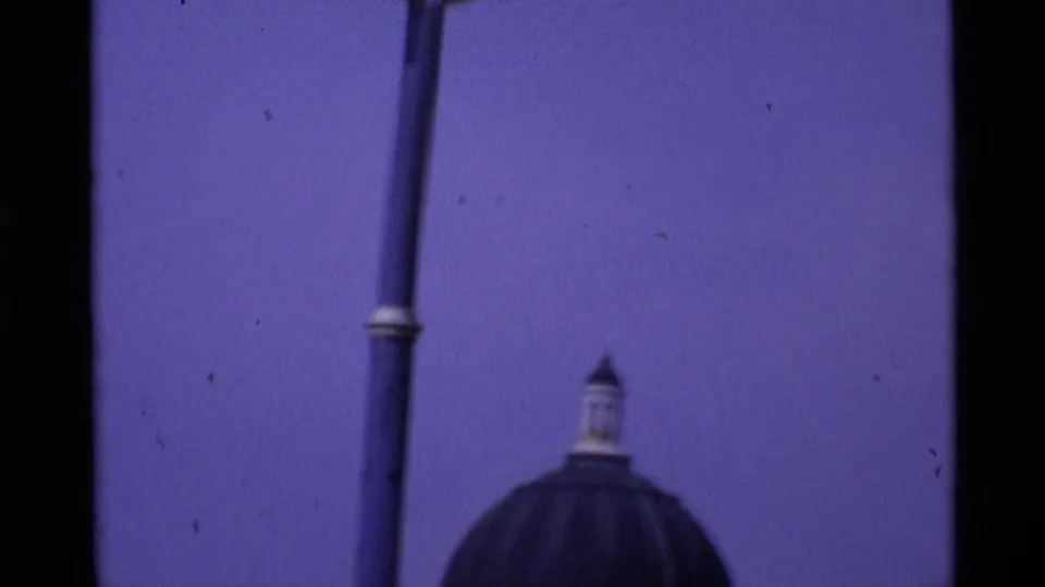 Soft 1969 London 8mm frame with a domed roofline, tall street pole, and faded blue-purple sky.