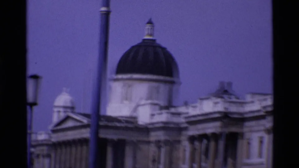 1969 London home-movie frame showing a domed classical building, partial columned facade, and street lamps in soft focus.