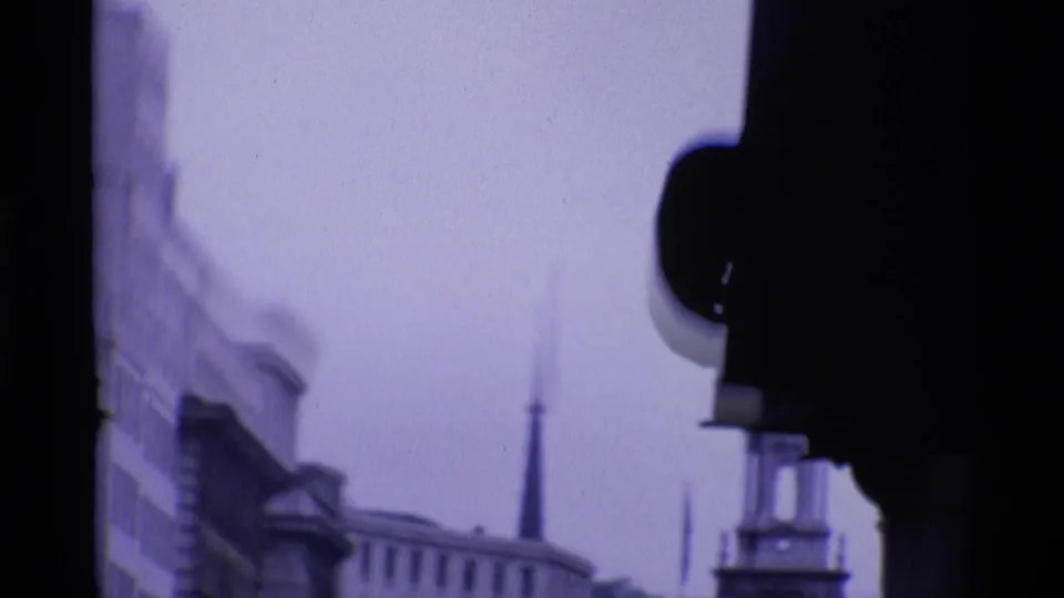 Soft 1969 London home-movie frame with blurred building edges, a distant steeple-like form, and dark foreground shapes.
