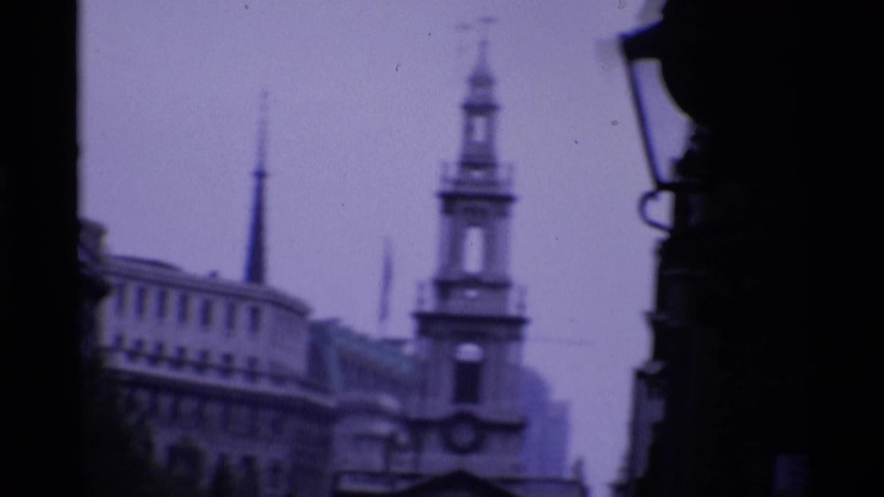 1969 London 8mm frame looking through a dark foreground edge toward a church spire and surrounding city buildings.