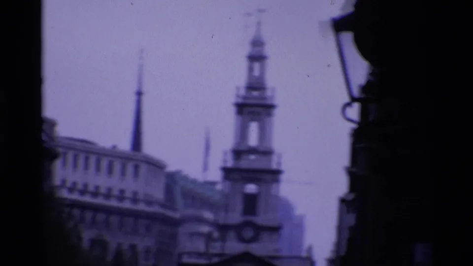 1969 London 8mm frame looking through a dark foreground edge toward a church spire and surrounding city buildings.