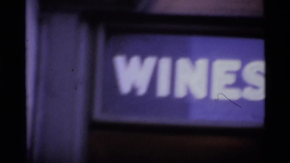 1969 London 8mm frame with a blurred shopfront sign reading “WINES” beneath the upper street scene.