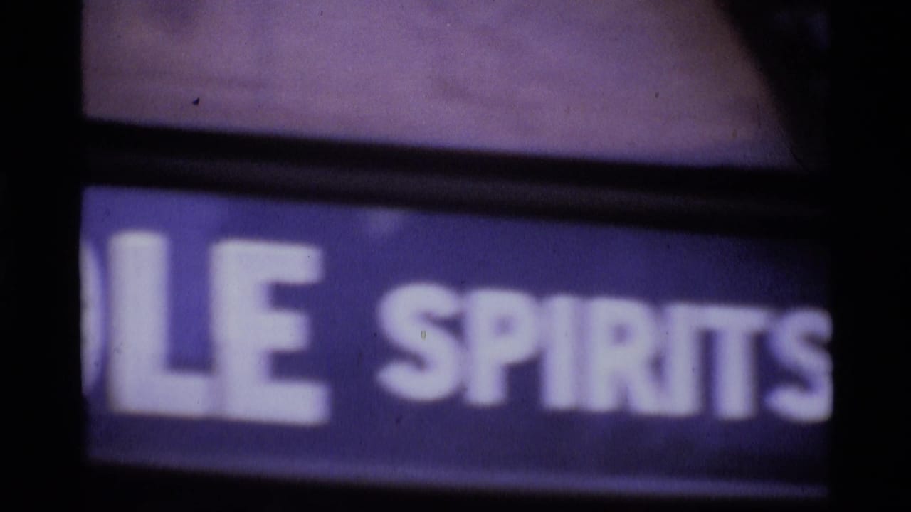 1969 London home-movie frame showing a soft, cropped sign with partial spirits lettering and dark surrounding edges.