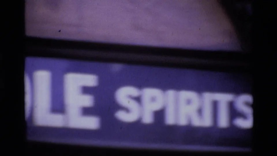 1969 London home-movie frame showing a soft, cropped sign with partial spirits lettering and dark surrounding edges.