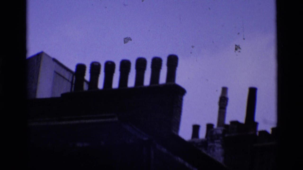 1969 London rooftop silhouette with clustered chimney pots and a purple-tinted sky in grainy 8mm footage.