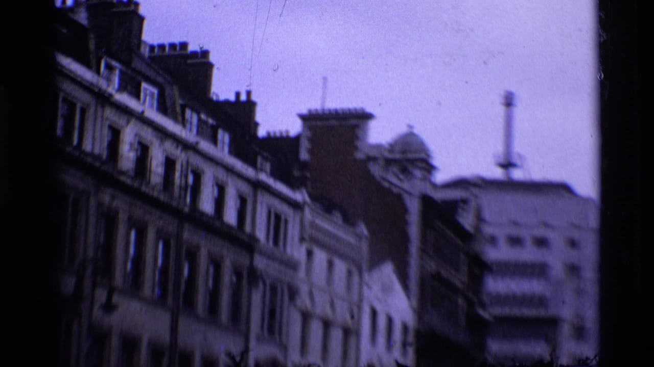 London street view on 8mm film, with older buildings, chimneys, and a blurred commercial facade in 1969 footage.