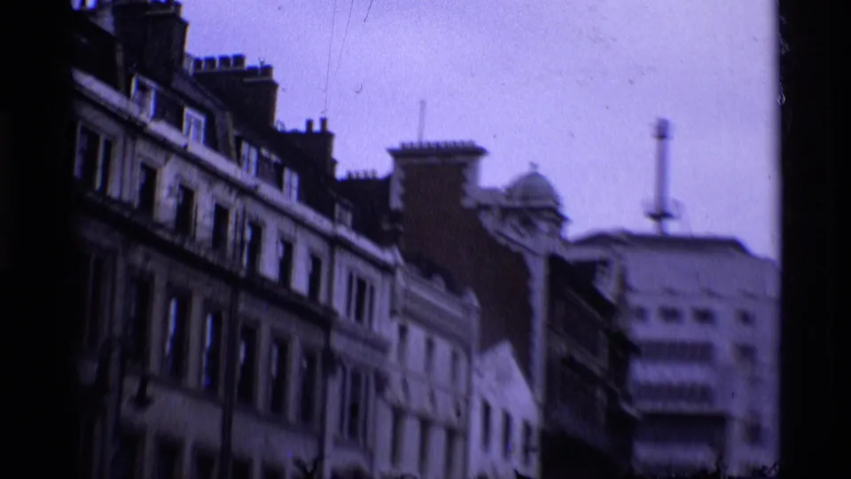 London street view on 8mm film, with older buildings, chimneys, and a blurred commercial facade in 1969 footage.