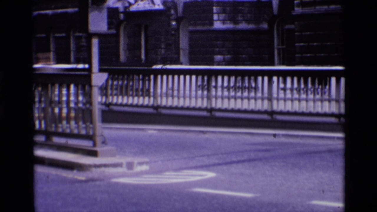 Street-level bridge railing with white road markings and masonry buildings beyond.