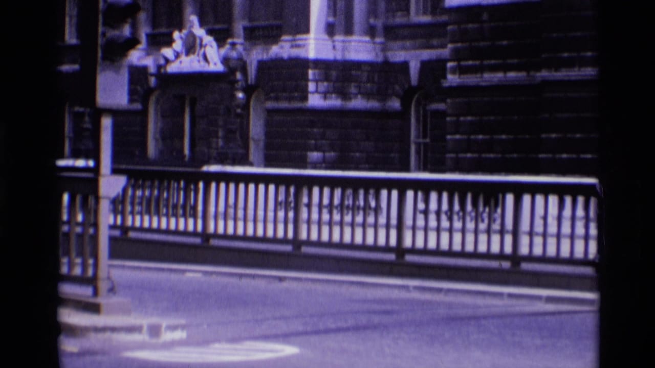 1969 London frame with metal bridge railings, quiet roadway, and an ornate building facade visible behind the street.