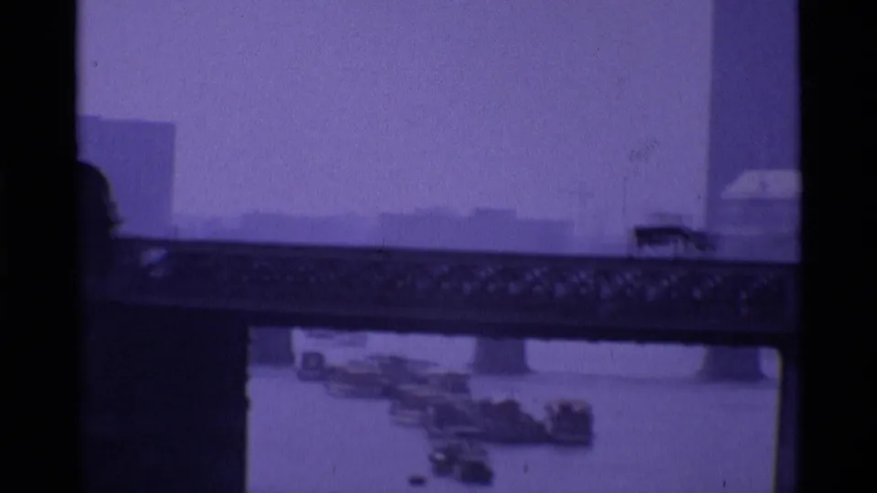 Purple-tinted 1969 London frame showing a hazy tower, bridge structure, and water below from a home-movie viewpoint.
