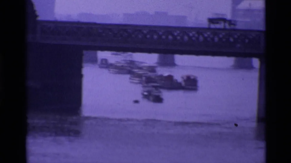 1969 London frame with a road bridge across the Thames and several small boats visible below in a purple-tinted home-movie scan.