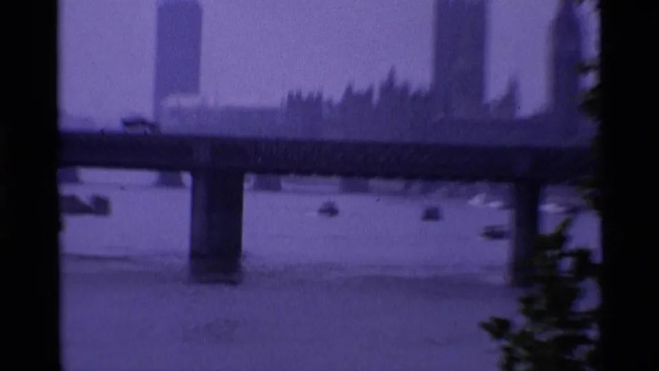 1969 London frame showing a Thames bridge, small boats, and a distant clock-tower silhouette through haze, consistent with supplied metadata.