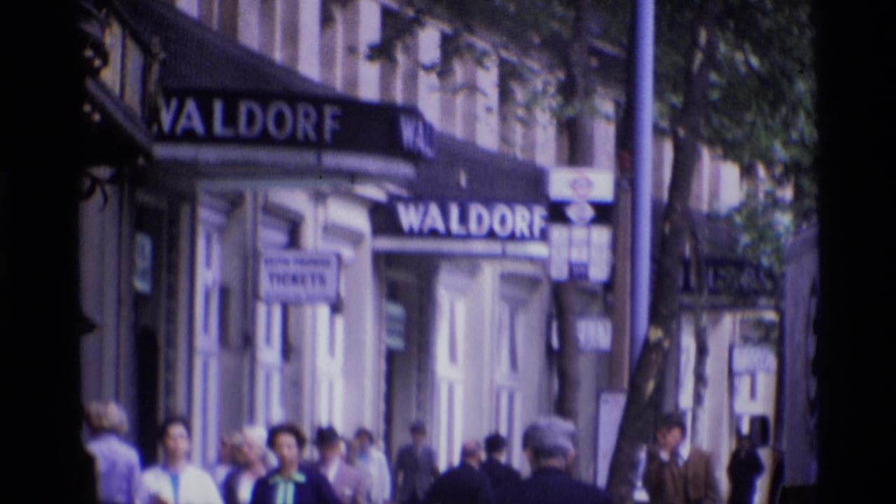 Pedestrians pass beneath Waldorf awnings on Aldwych in a soft, handheld 1969 London street view.
