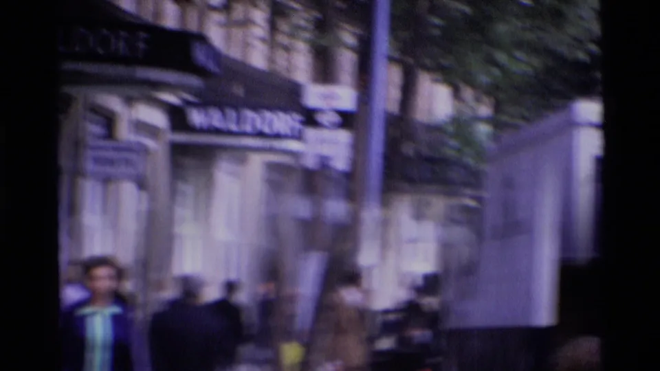 A handheld 8mm view catches pedestrians and the Waldorf awning in motion blur along Aldwych, London.