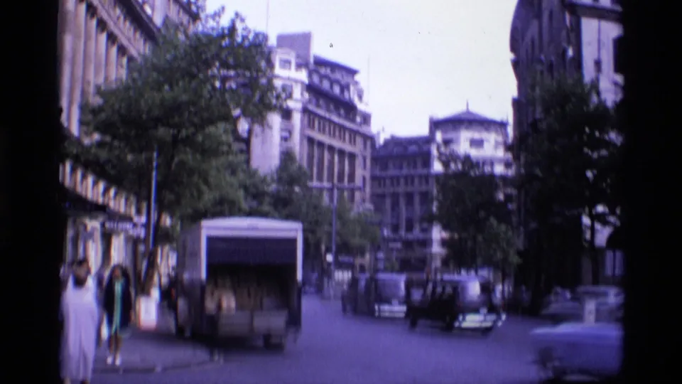 Wide 1969 Aldwych street view with pedestrians, a delivery truck, trees, building facades, and classic cars in traffic.