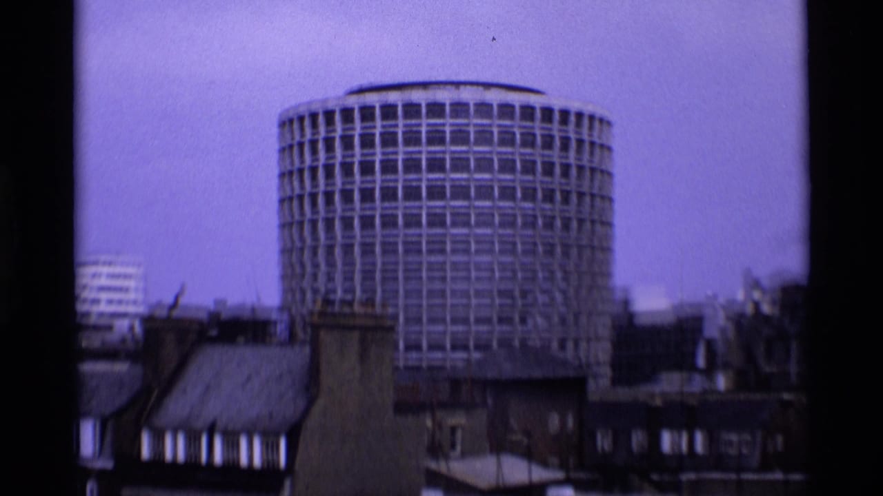 Circular modern London building seen above lower rooftops, filmed with a cool purplish 8mm cast.