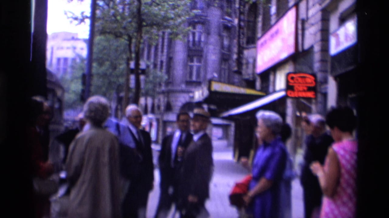 1969 London sidewalk scene with adults in suits and dresses gathered near a hotel entrance and street-facing shops.