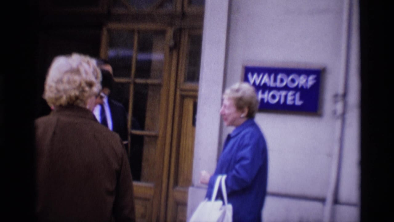 Adults linger and talk outside the Waldorf Hotel entrance in London, with the blue hotel sign visible on the wall.