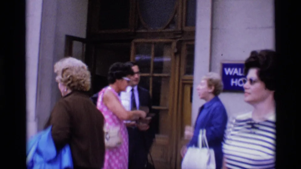 Adults in 1960s clothing move and converse outside the Waldorf Hotel entrance in London.