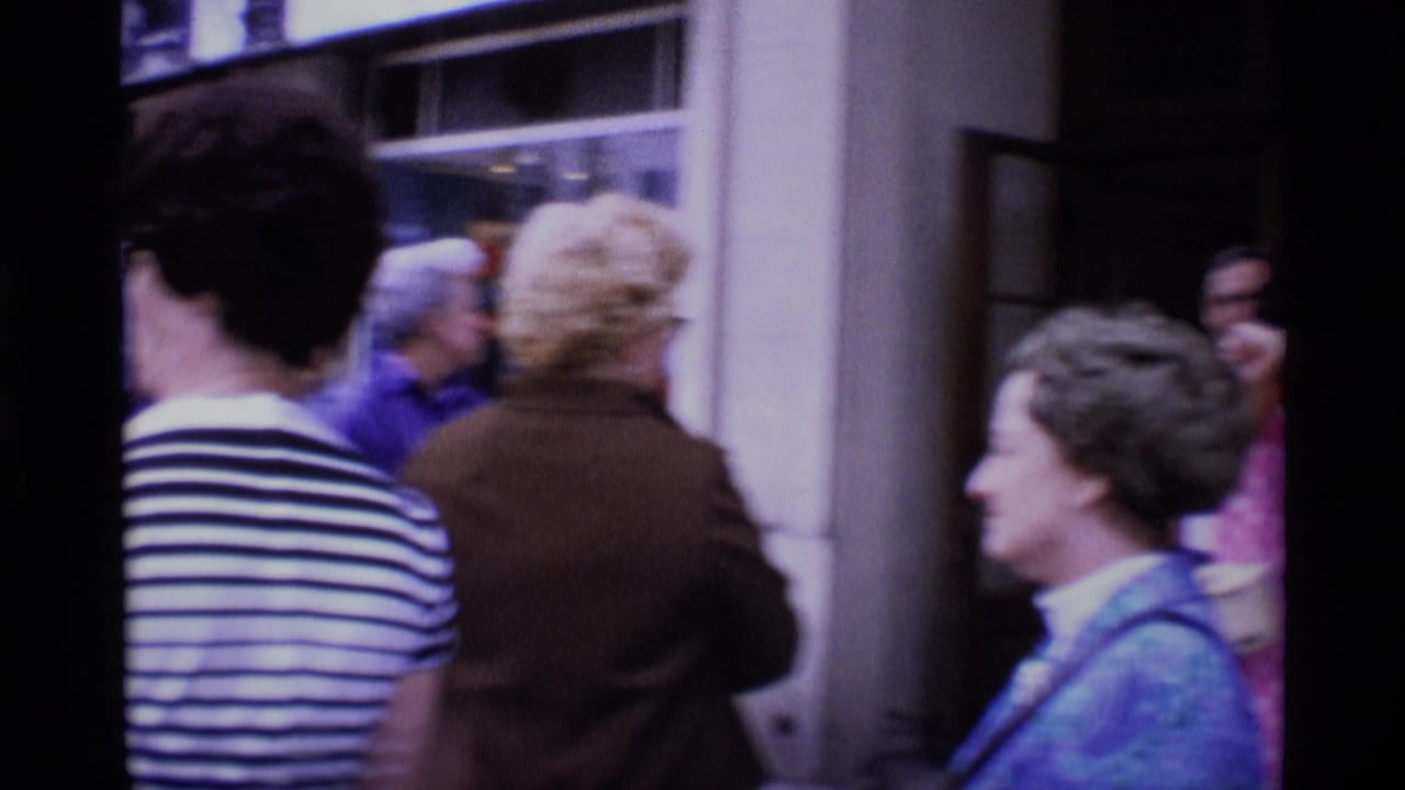 Crowd near a shop window and hotel frontage, seen from a handheld street-level view.