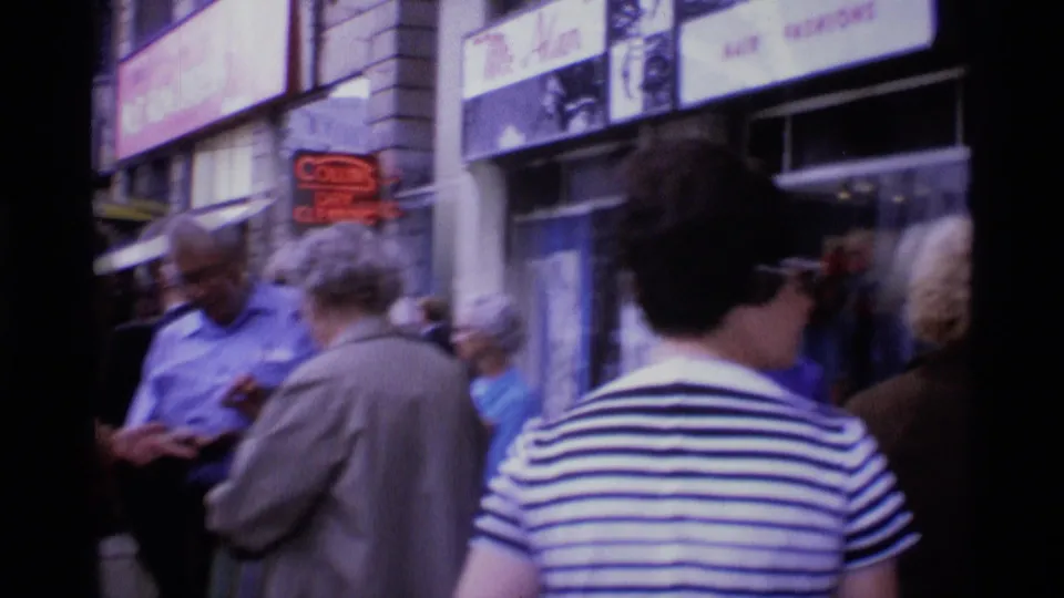 1969 London pavement scene with pedestrians passing storefronts, including a visible dry-cleaning sign.