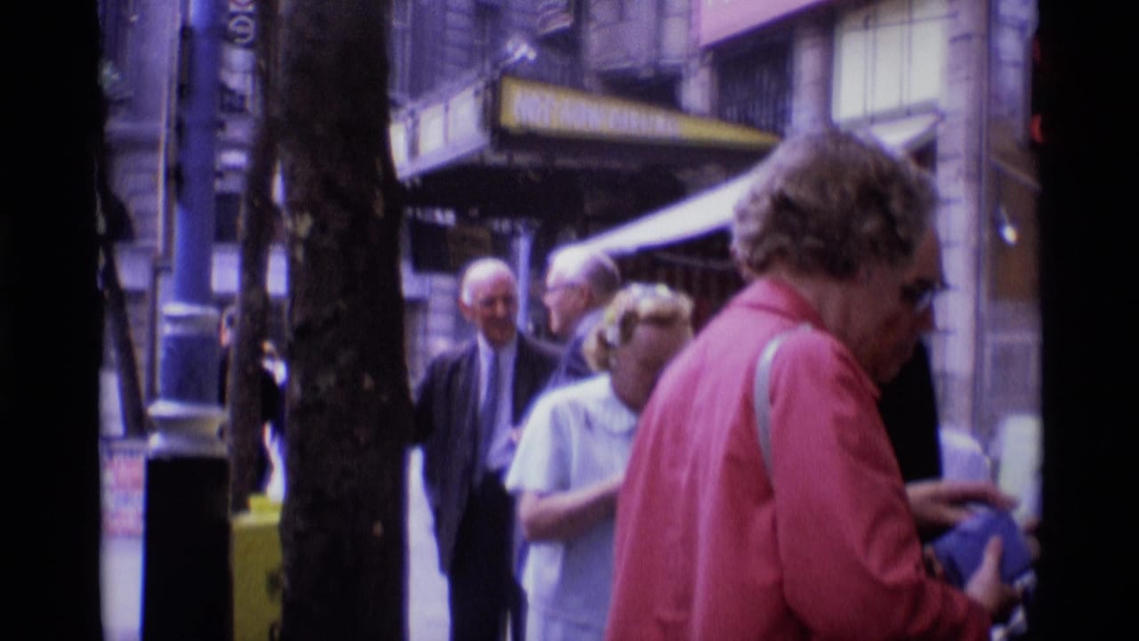 Older adults stand and pass on a London sidewalk near tree trunks and shop awnings.