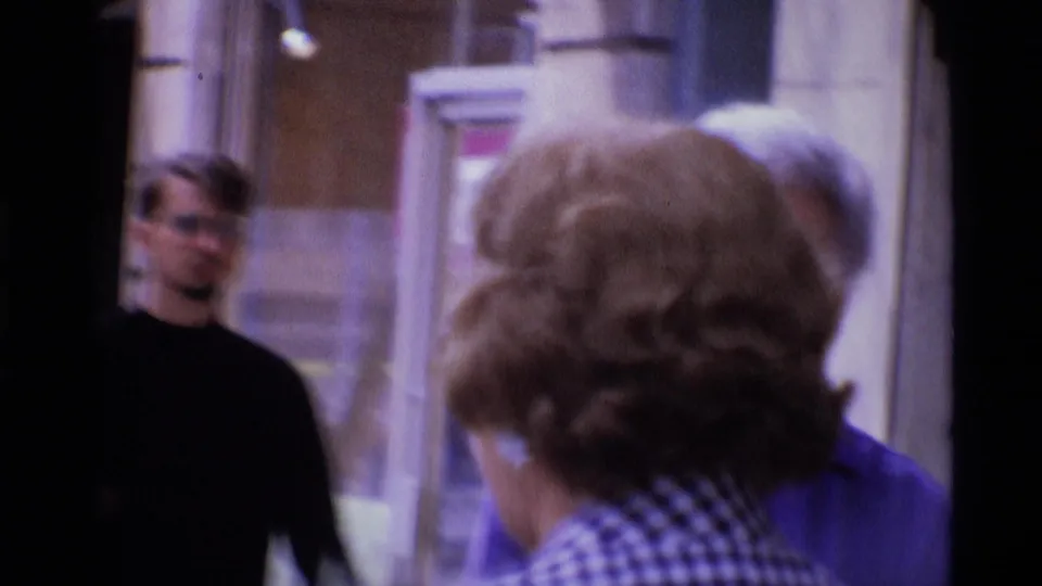 London 1969 bus frame showing an older passenger from behind near the window, with another face visible beyond the glass.