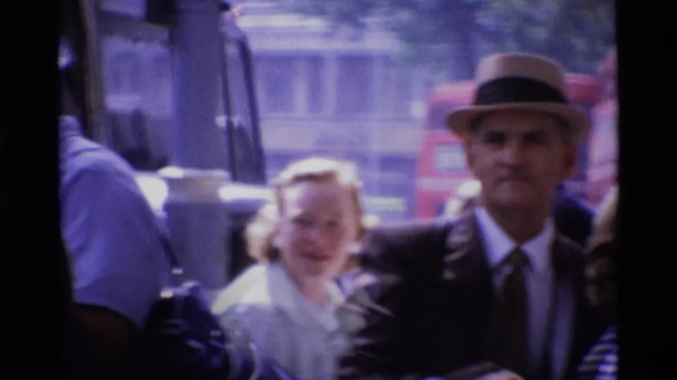 1969 London street frame with a man in a brimmed hat near pedestrians and blurred traffic in the background.