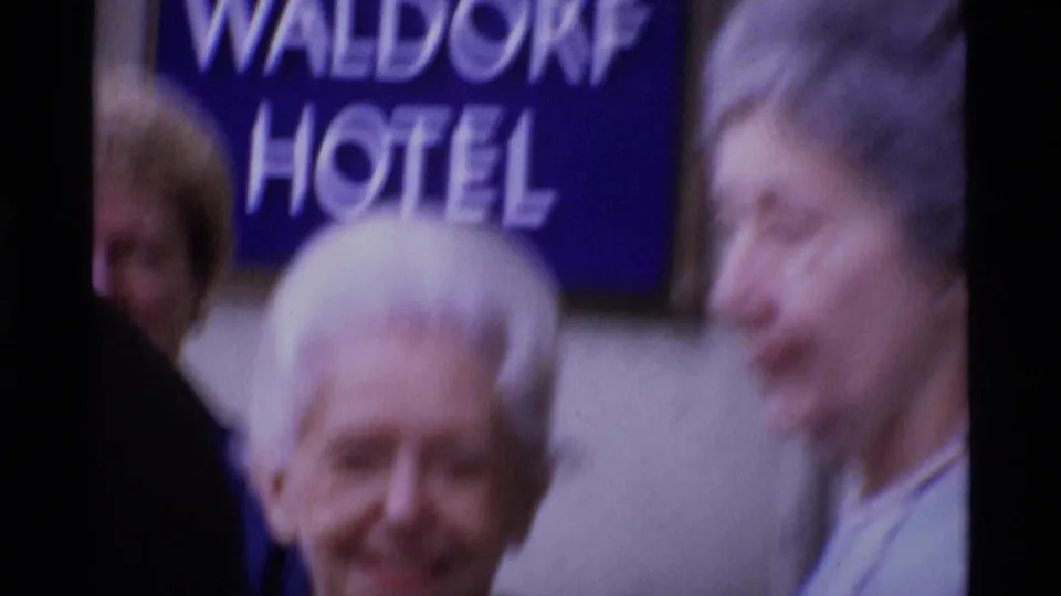 Soft 8mm close view outside the Waldorf Hotel in London, with adult faces and the blue hotel sign partly visible.