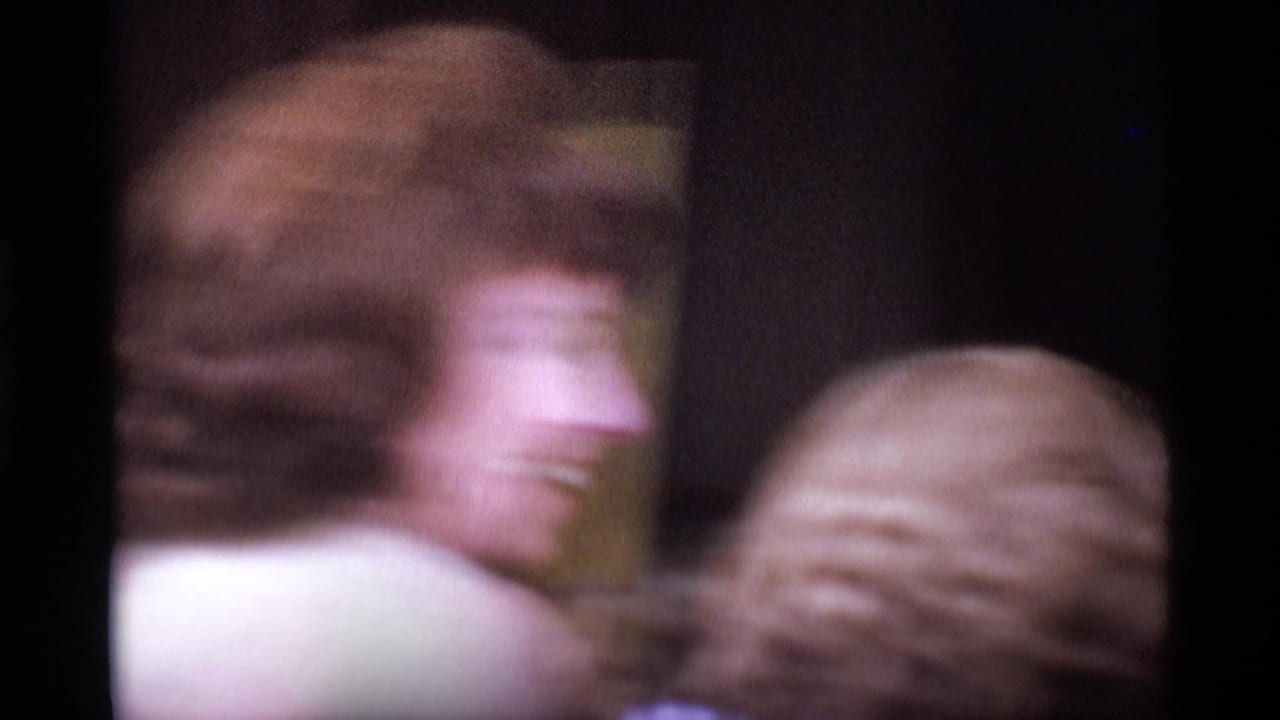 Soft 8mm frame from 1969 London showing blurred adults close to the camera in a busy public space.