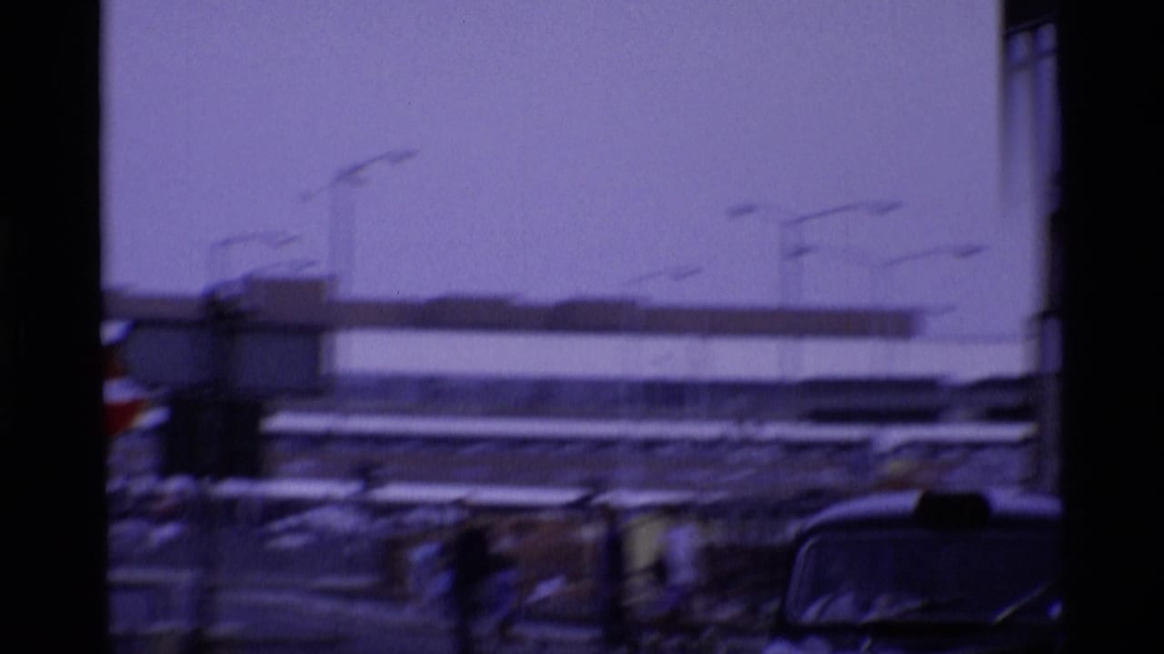 Blurred street view with parked cars and a large modern building beyond the roadway.